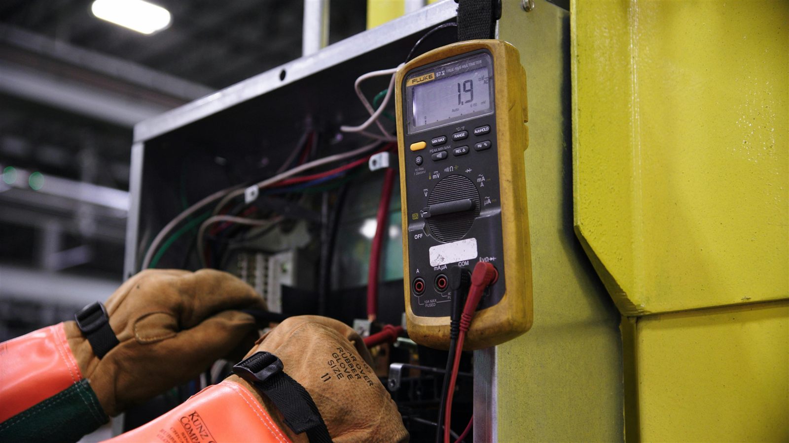 Technician using a digital multimeter to test electrical components in a commercial control panel