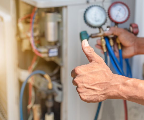 HVAC technician giving thumbs up while holding refrigerant gauges during air conditioning service