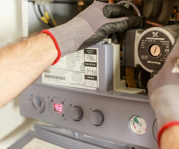HVAC technician in work gloves inspecting internal components of a boiler or water heater